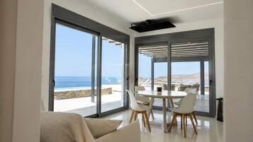 A modern interior with large sliding glass doors, a round dining table, white chairs, and a sofa with a checkered throw.