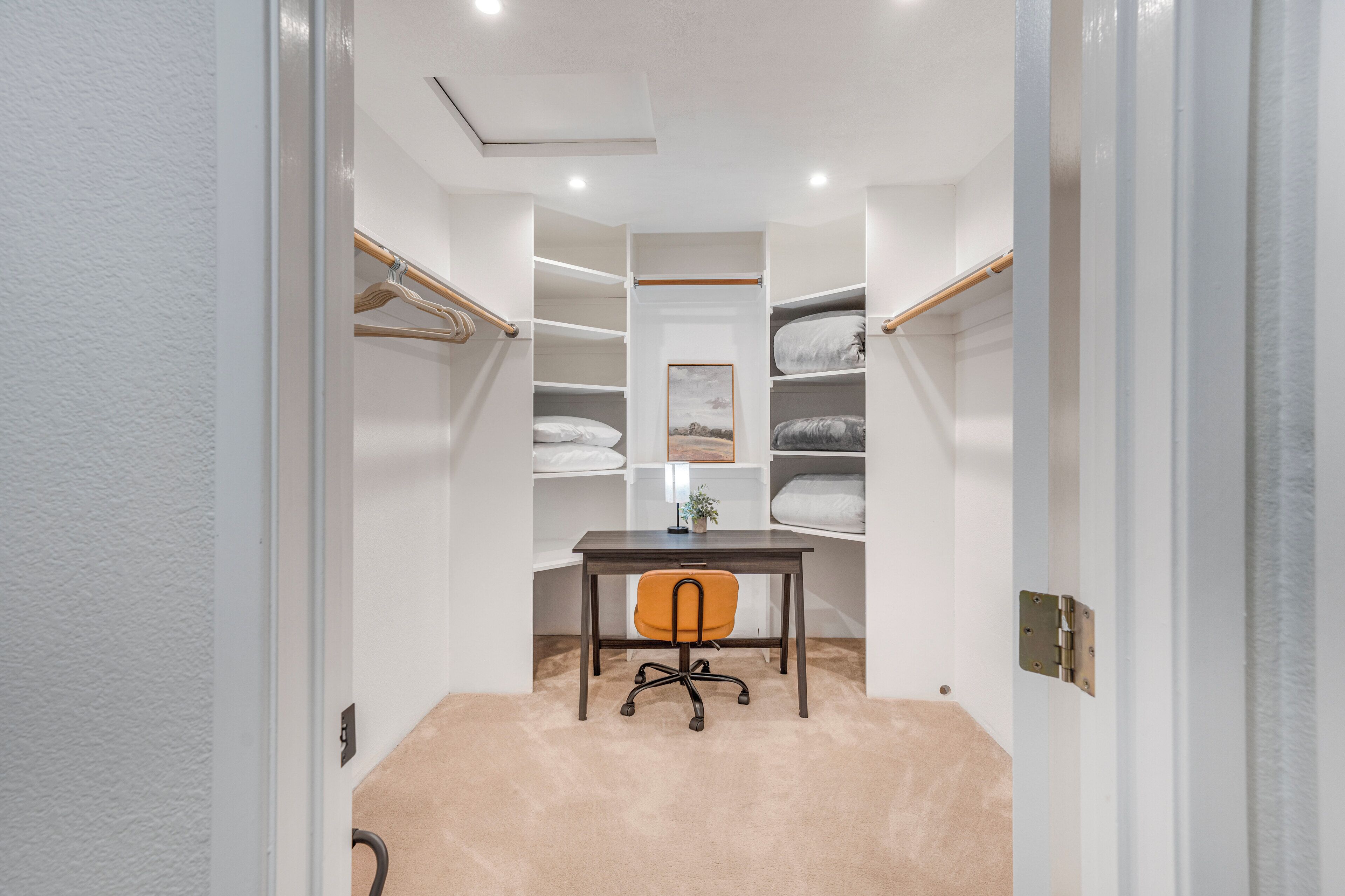 A walk-in closet with shelves, a desk, and an orange chair.