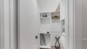 A narrow hallway with a white door, a white wall, and a small shelf with a folded garment and a small item.