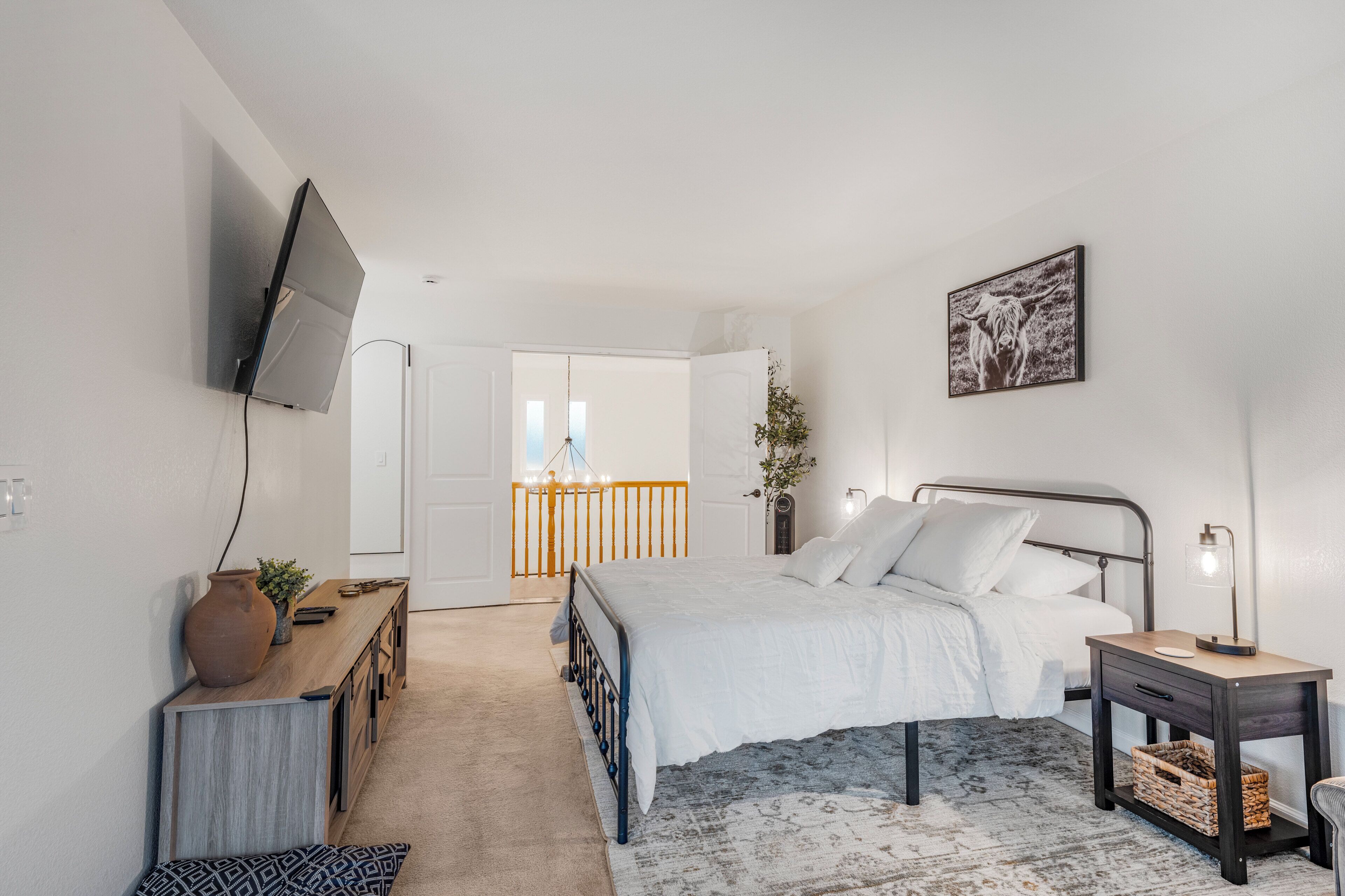 Quarto com cama, mesa de cabeceira, abajur, televisão e vista para uma varanda.
