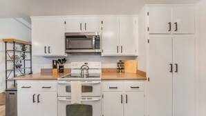 A kitchen with white cabinets, a microwave, stove, oven, and a countertop with a kettle.