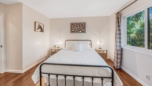 A bedroom with a bed, bedside tables, a wall-mounted artwork, a window with curtains, and a door.