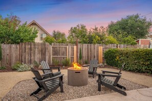 A backyard with a fire pit, outdoor seating, a wooden fence, and a house in the background.