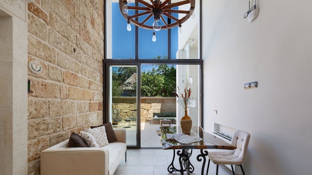 A modern interior with a stone wall, a white sofa, a glass door leading outside, and a table with chairs. - Domus Sagari - Suite Executive (Presicce)