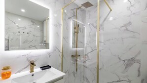 A bathroom with a white marble sink, a mirror, and a glass-enclosed shower with gold fixtures. - PERFECTLY POSITIONED FOR DISCOVERING THE CITY'S VIBRANT ATMOSPHERE ON FOOT (Cannes)