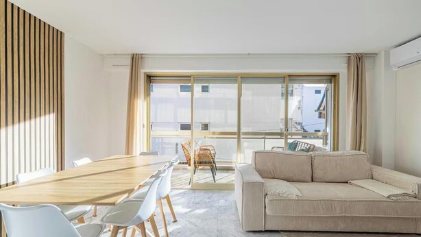 A modern living room with a wooden dining table, white chairs, a beige sofa, and large windows. - PERFECTLY POSITIONED FOR DISCOVERING THE CITY'S VIBRANT ATMOSPHERE ON FOOT (Cannes)