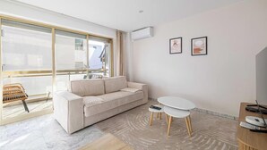 A modern living room with a sofa, a small round table, a TV, and a window with a view. - PERFECTLY POSITIONED FOR DISCOVERING THE CITY'S VIBRANT ATMOSPHERE ON FOOT (Cannes)