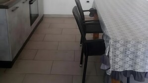 Eine Küche mit Herd, Backofen und Schränken, einem Esstisch mit Stühlen sowie einer Tür.