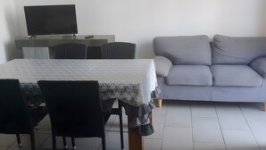 Ein Wohnzimmer mit Esstisch, Stühlen, einer Couch, einem Fernseher und einer Wanduhr.