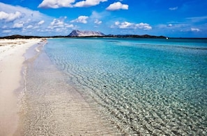 Ein Strand mit klarem türkisblauem Wasser, einem Sandufer und einem Berg im Hintergrund.