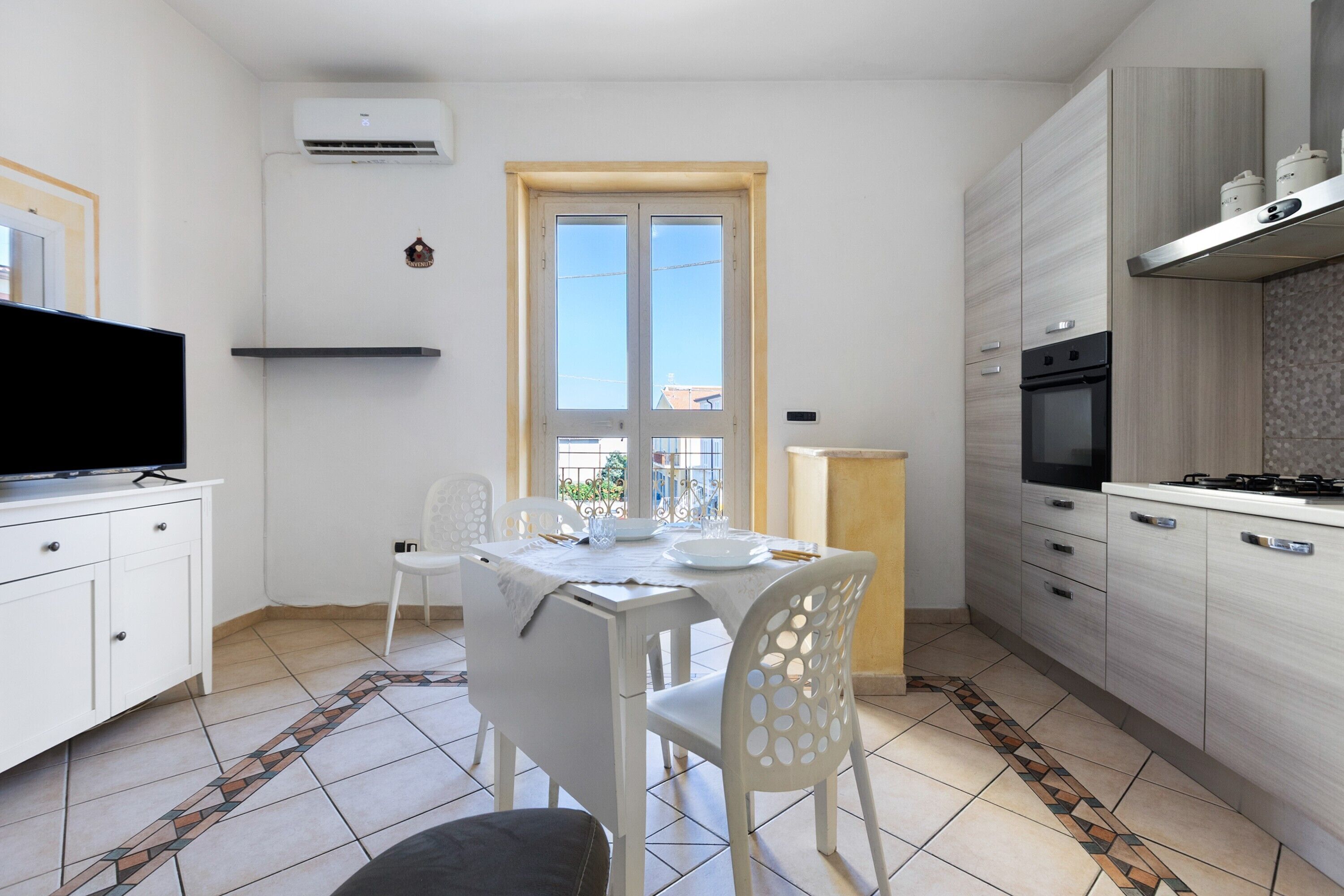 Una cucina moderna con mobili bianchi, forno integrato e zona pranzo con tavolo e sedie.