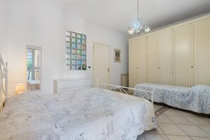 A bedroom with a large bed, two smaller beds, a wardrobe, a mirror, and a picture on the wall.