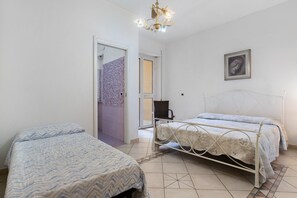 Une chambre avec deux lits, un lustre, un tableau encadré au mur et une porte donnant sur une salle de bain.