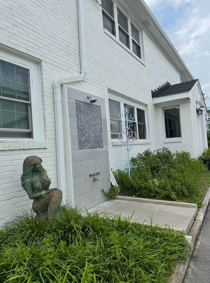 A white building with a door, a small garden, and a statue.