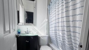 A bathroom with a toilet, sink, mirror, and shower curtain. - The SEA-renity 16 cozy apartment across from the beach (Norfolk)