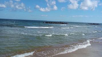 Una playa con olas, cielo despejado y un muelle a lo lejos.