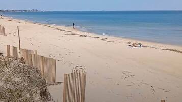 A sandy beach with a wooden fence and a person walking.