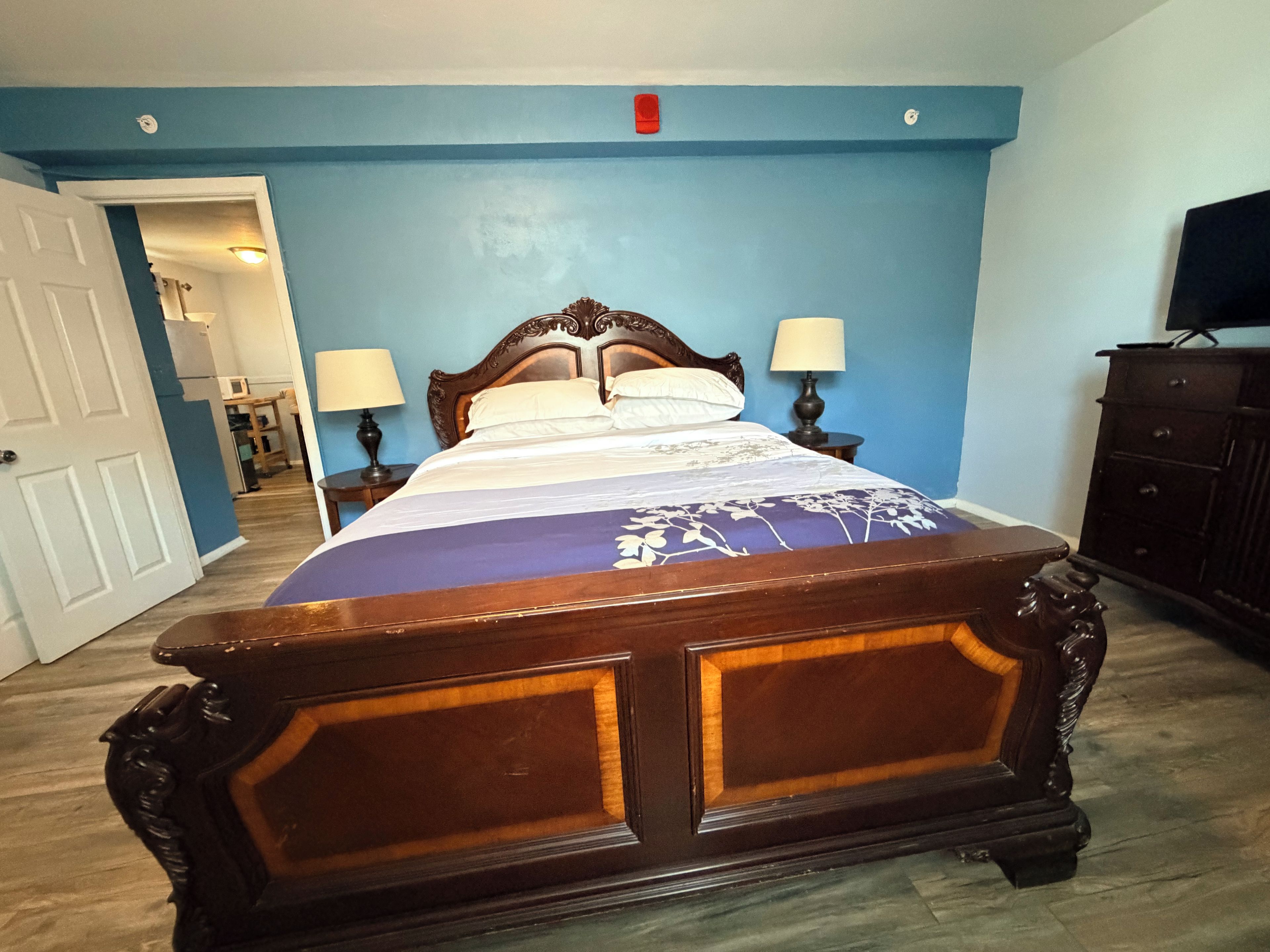 A bedroom with a wooden bed, two bedside lamps, a dresser, and a television on a stand.