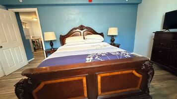 A bedroom with a wooden bed, two bedside lamps, a dresser, and a television on a stand.