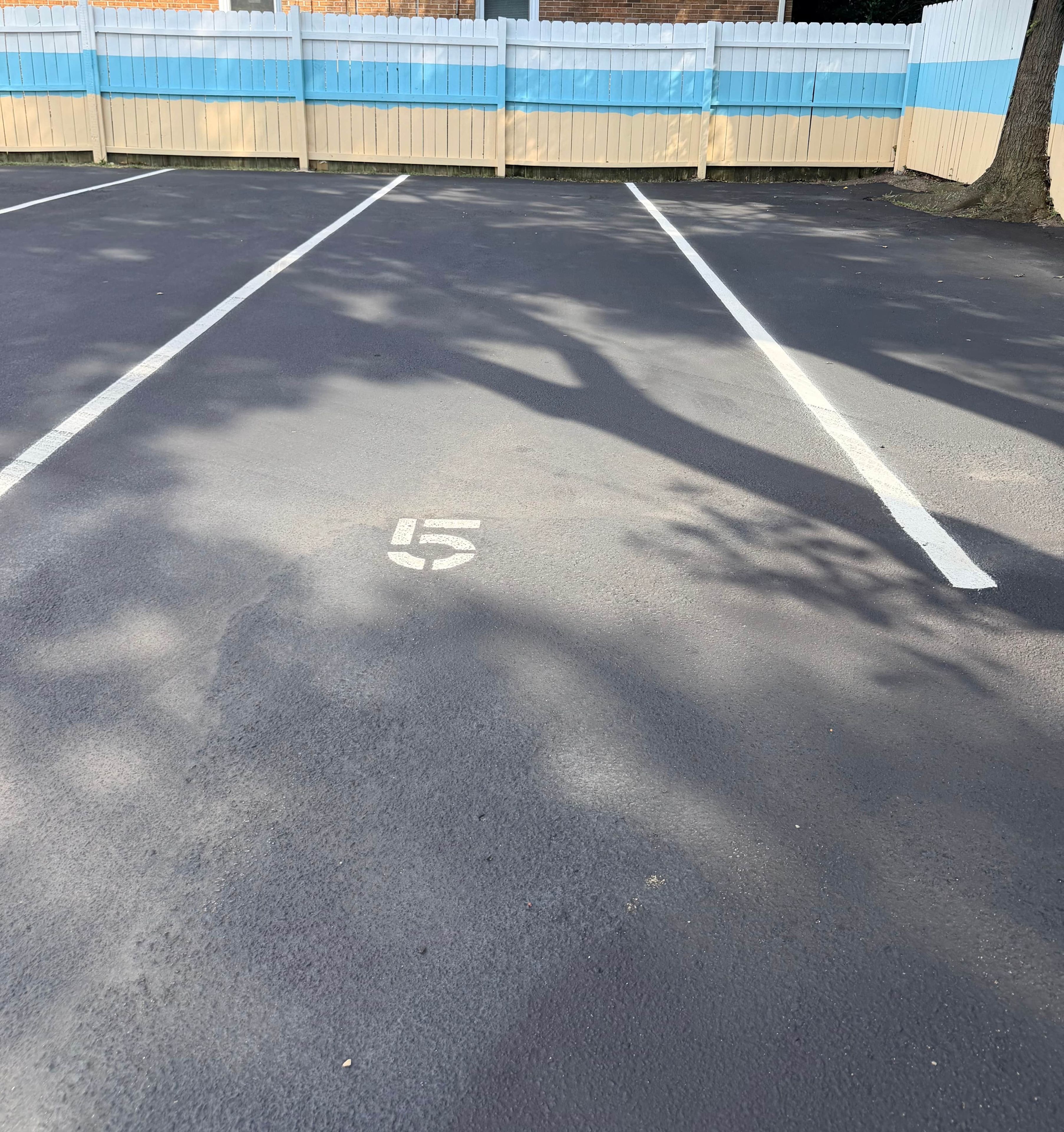 Un estacionamiento con espacios delimitados y una cerca blanca al fondo.
