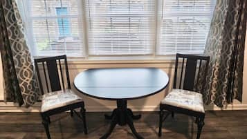 Een ronde tafel met twee stoelen, een raam met zonwering en behang.