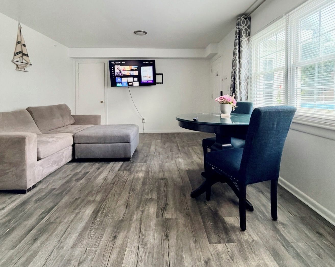 Een moderne woonkamer met een grijze modulaire bank, een ronde eettafel met een blauwe stoel en een flatscreen televisie aan de muur.