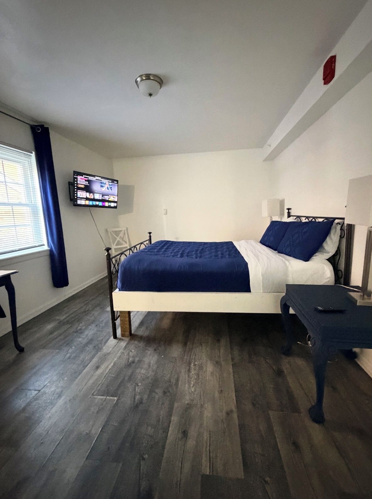 Een slaapkamer met een bed, een aan de muur bevestigde televisie en een raam met gordijnen.