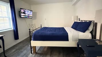 Een slaapkamer met een bed, een aan de muur bevestigde televisie en een raam met gordijnen.