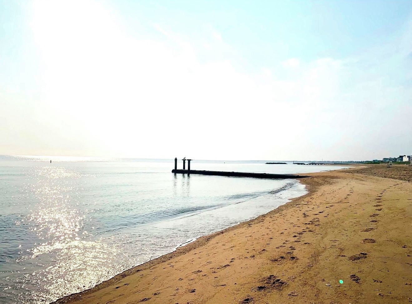 Una playa con un muelle que se adentra en aguas tranquilas, orilla arenosa y cielo despejado.