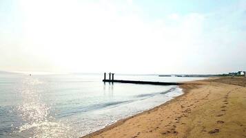 Una playa con un muelle que se adentra en aguas tranquilas, orilla arenosa y cielo despejado.