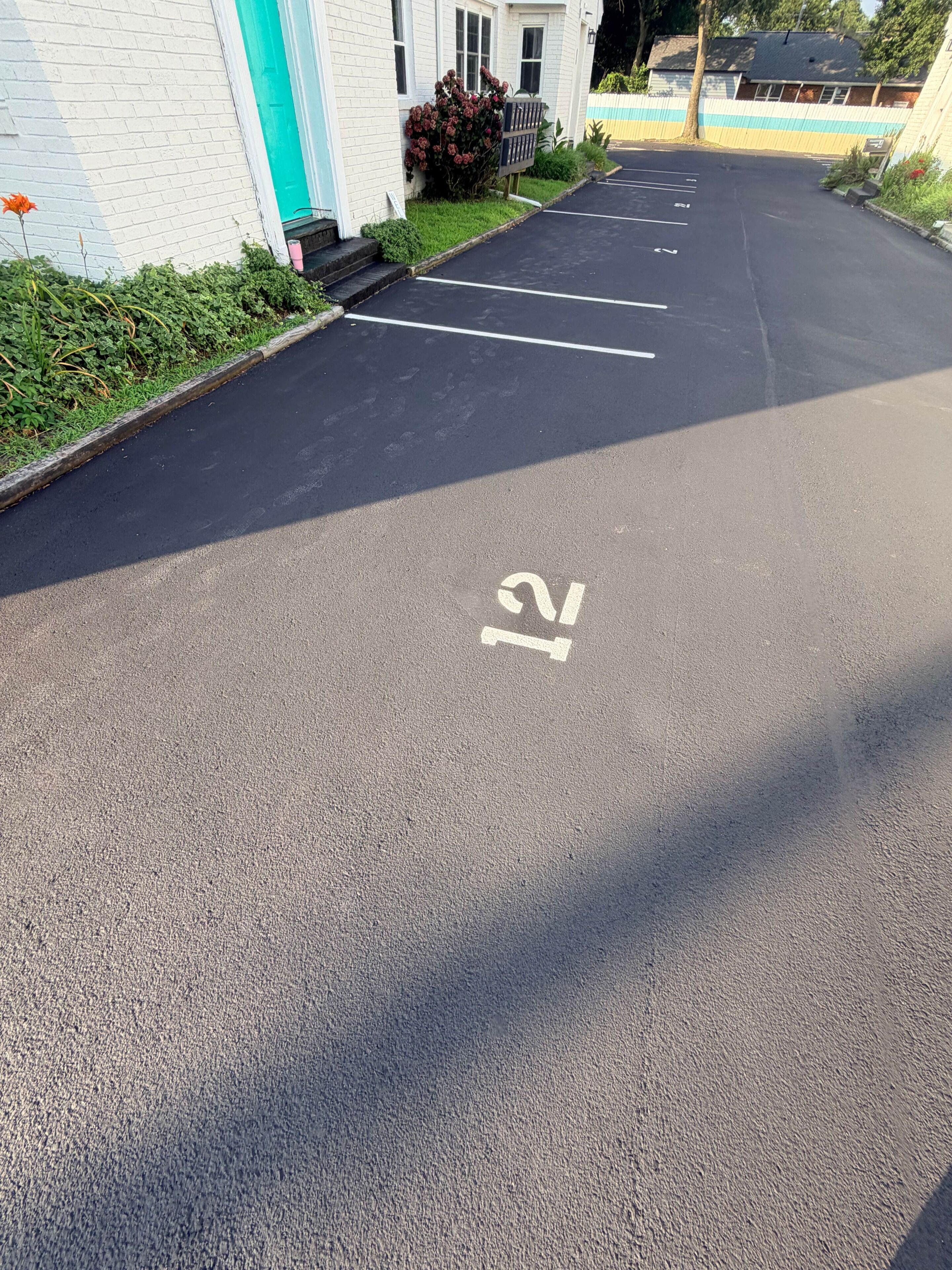 Een parkeerplaats met aangegeven parkeerplaatsen en een gebouw met een witte gevel en een groene deur.