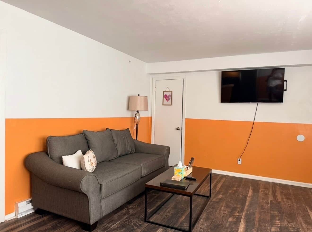 Een woonkamer met een bank, een salontafel, een lamp en een televisie aan de muur.