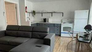 Ein Wohnzimmer mit einem Ecksofa, einem Glastisch zum Essen und einer Küchenzeile mit Geräte.