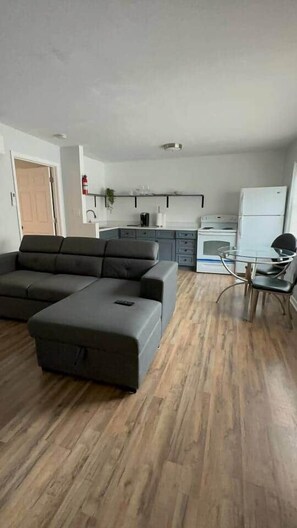A living room with a sectional sofa, a glass dining table, and a kitchen area with appliances. - SEA-renity 13 cozy apartment across from the beach (Norfolk)