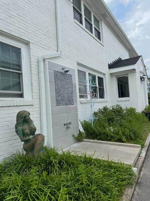 Une maison en briques blanches avec une porte d’entrée, un petit jardin et une statue de femme.