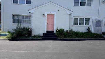 Un bâtiment à deux étages avec une porte rose, des murs en briques blanches et un petit porche avec des marches.