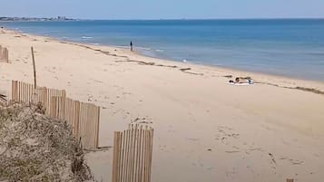 A sandy beach with a wooden fence and a person walking.