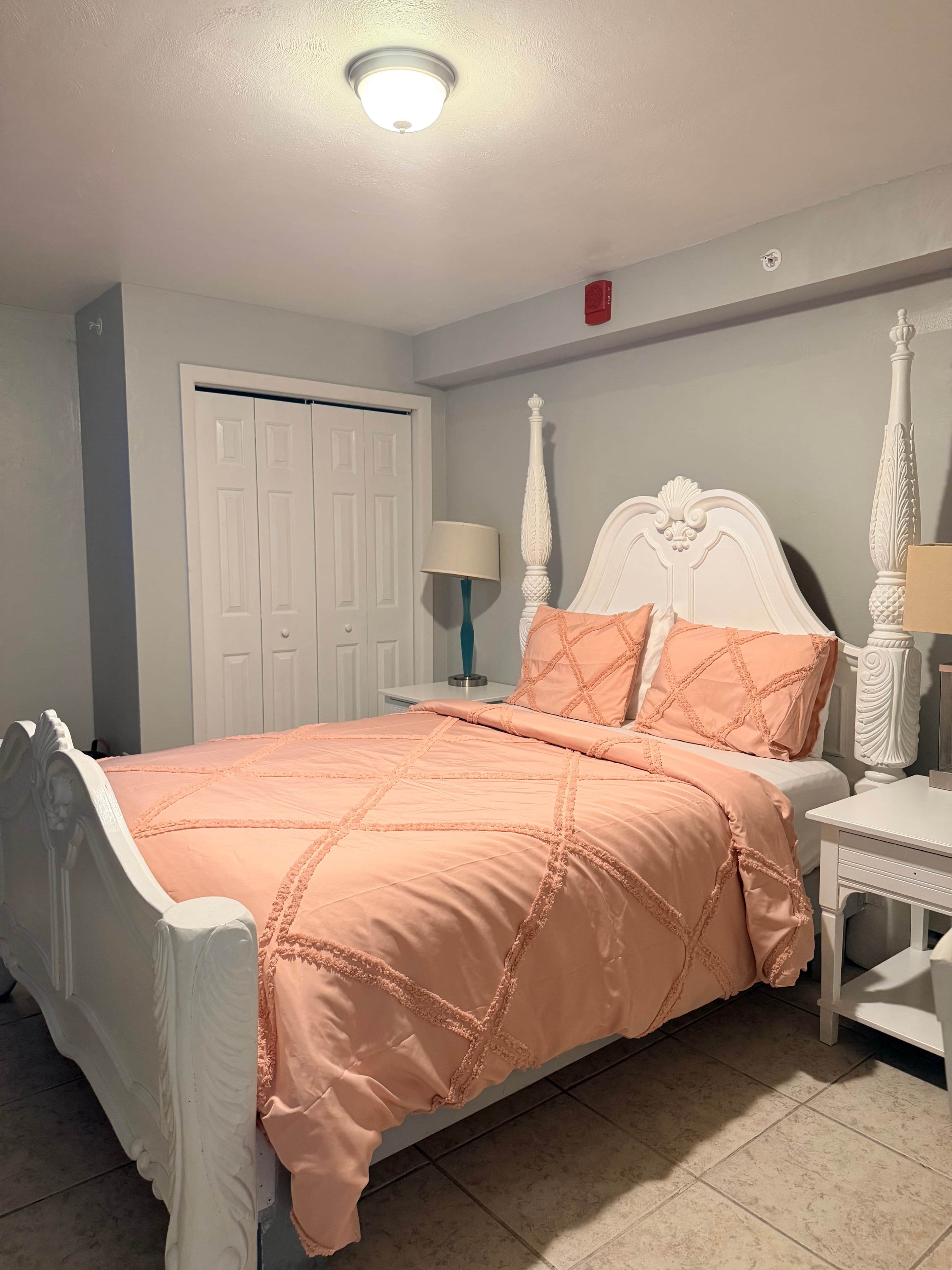 A bedroom with a bed, nightstand, lamp, and a door.