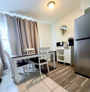 A compact kitchen with a dining table, chairs, a refrigerator, and a microwave. - The SEA-renity 15 cozy apartment across from the beach (Norfolk)