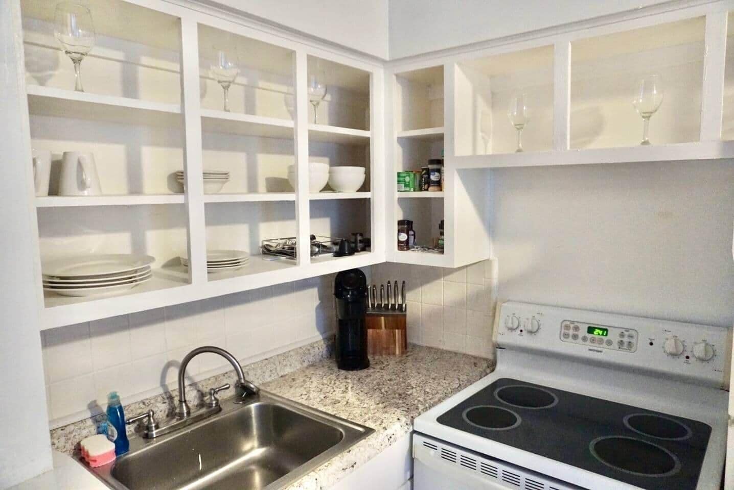 A kitchen with white cabinets, a stainless steel sink, a stove, and various kitchen utensils.