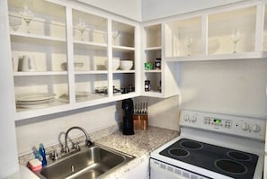 A kitchen with white cabinets, a stainless steel sink, a stove, and various kitchen utensils. - The SEA-renity 11 cozy apartment across from the beach (Norfolk)