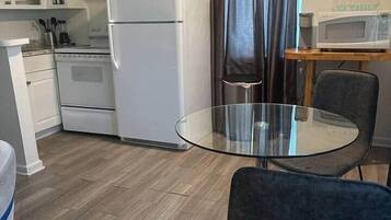 A compact kitchen with white appliances, a glass table, and a dark chair.