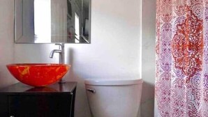Un bany amb un vàter blanc, un lavabo vermell, un moble de bany negre, un mirall i una cortina de dutxa amb un disseny decoratiu.