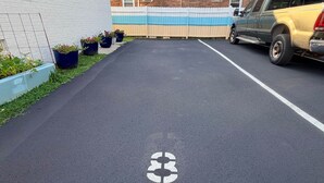 A parking area with a white line marking, a brick building, and a yellow vehicle parked.