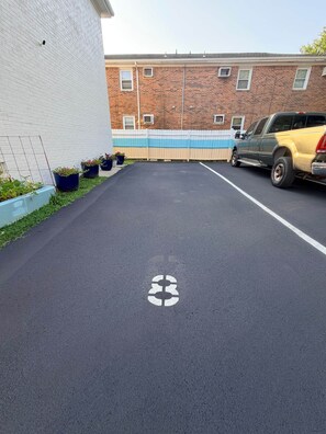 A parking area with a white line marking, a brick building, and a yellow vehicle parked. - The SEA-clusion 8 cozy apartment across from the beach (Norfolk)