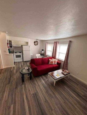 A compact living space with a red sofa, a small coffee table, and a kitchenette in the background. - The SEA-clusion 8 cozy apartment across from the beach (Norfolk)