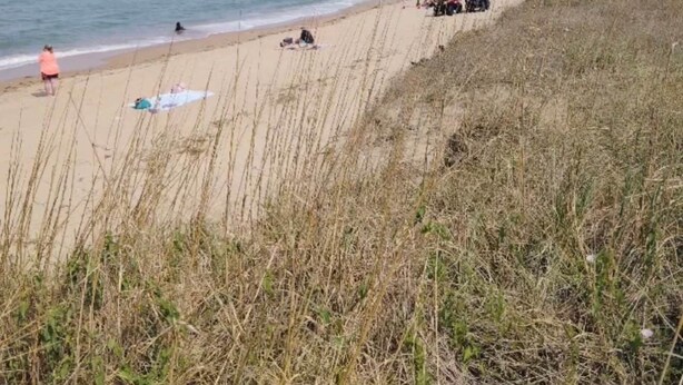 A beach with people and ATVs, a clear sky, and a calm sea.