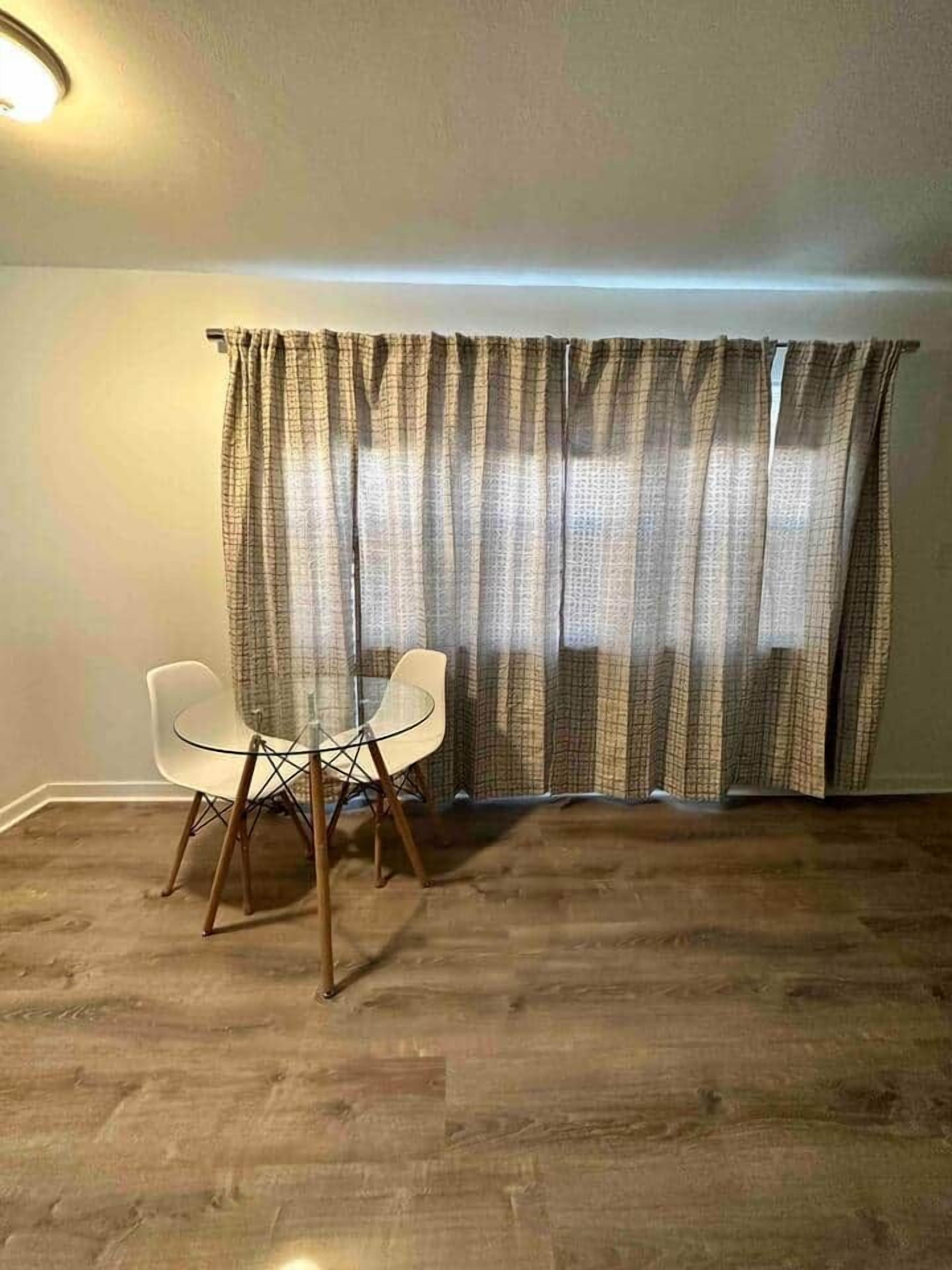 Een kamer met een eettafel en stoelen, een kamerbreed gordijn met patroon, en een houten vloer.