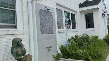 A white brick house with a front door, a small garden, and a statue of a woman.