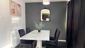 Un coin repas comprenant une table rectangulaire, des chaises noires, une plante en pot, un miroir et un radiateur.